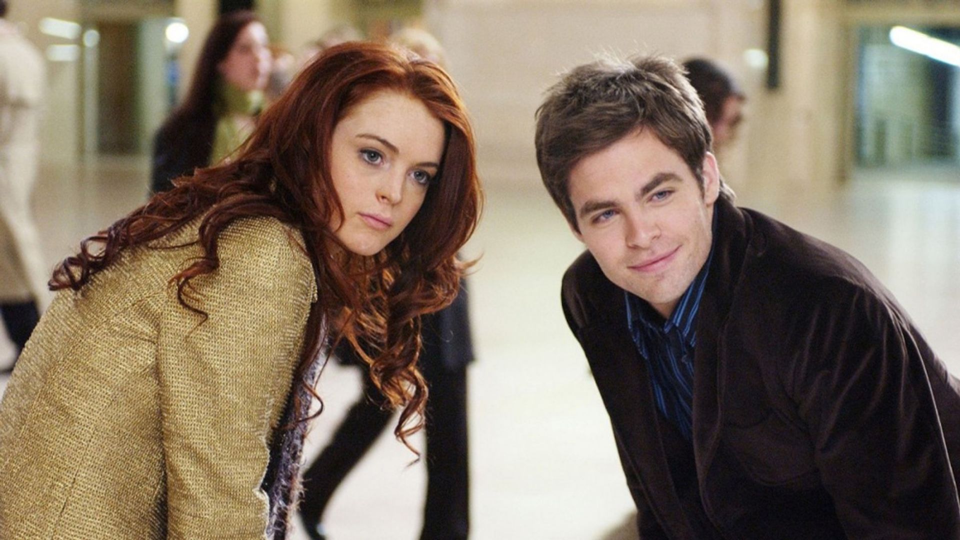 Lindsay Lohan e Chris Pine estão lado a lado, inclinando-se para a frente numa sala cheia de gente