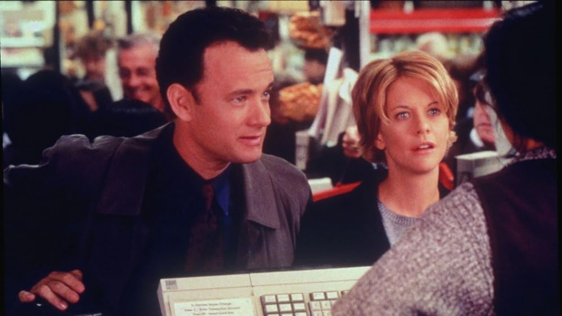 Tom Hanks e Meg Ryan de pé no balcão de uma loja, a falar com o funcionário