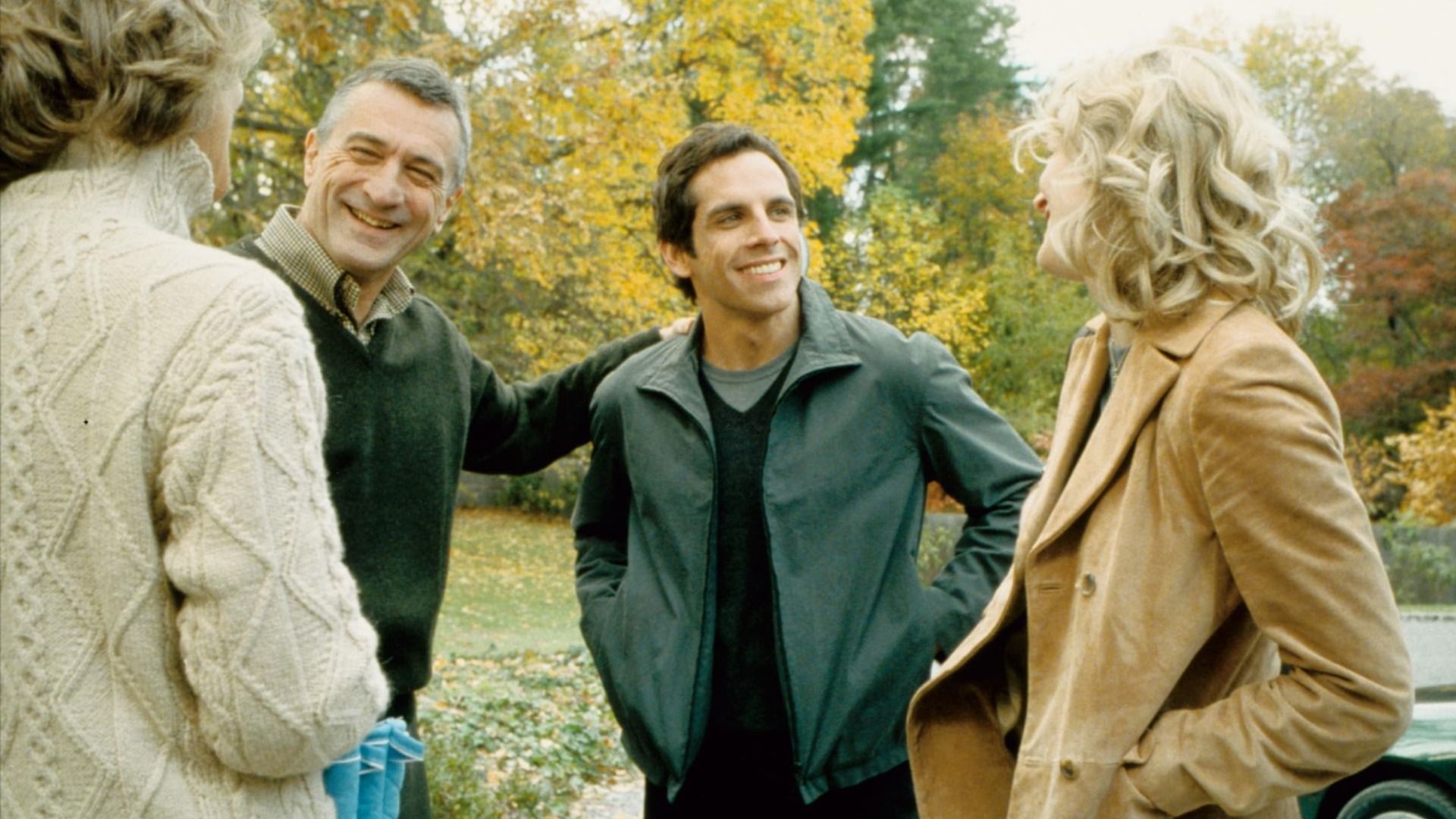 Os atores Robert De Niro numa camisola verde e Ben Stiller num casaco verde junto a árvores com folhas amarelas