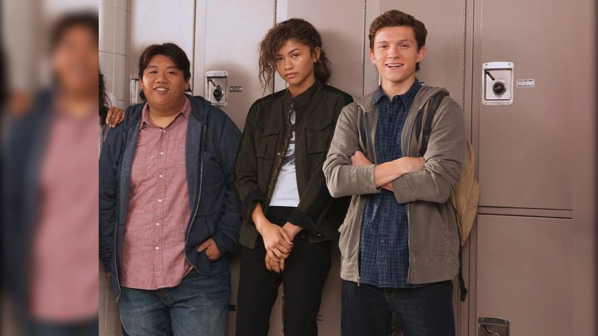 Os atores Jacob Batalon, Zendaya e Tom Holland em roupas casuais junto aos cacifos da escola