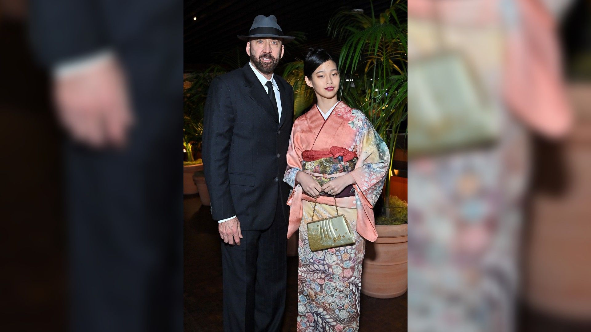 Nicolas Cage de fato preto e chapéu e Riko Shibata num quimono cor-de-rosa com padrões