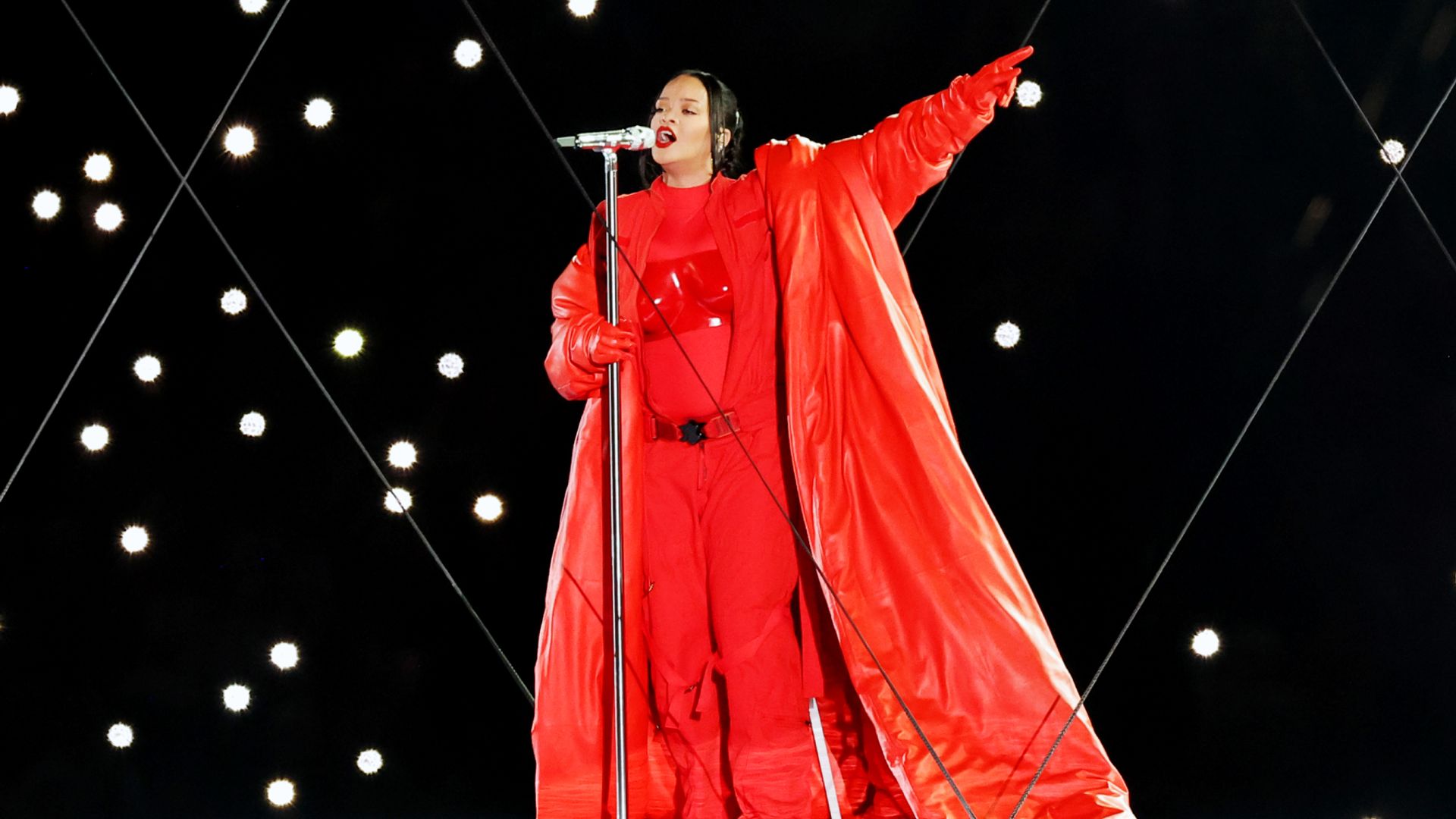 Rihanna num fato vermelho brilhante e capa comprida atua no palco com um microfone