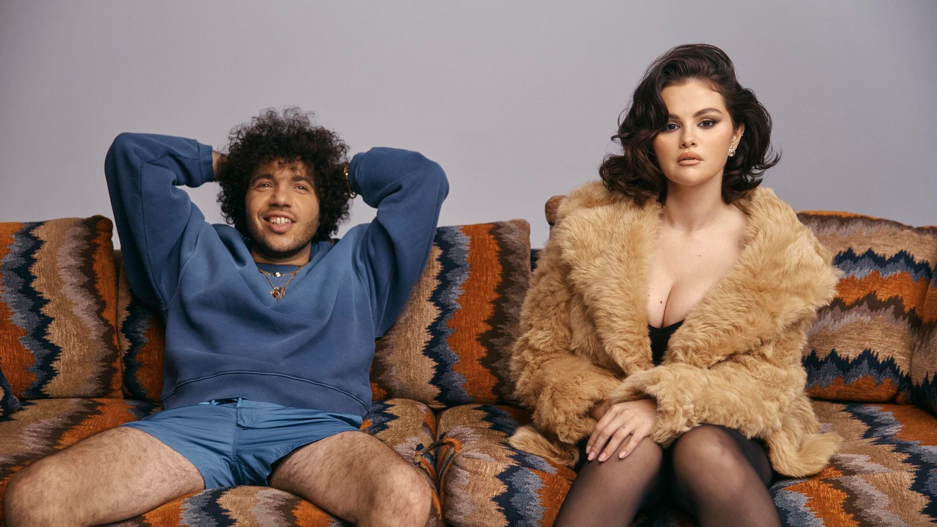 Selena Gomez num casaco de pele e Benny Blanco numa camisola azul e calções sentados descontraidamente