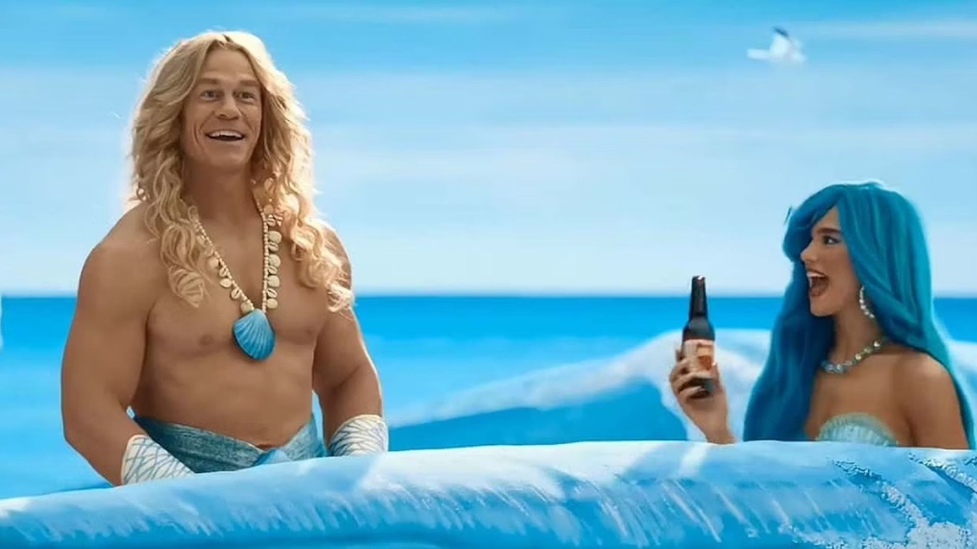 John Cena e Dua Lipa em fatos de sereia nadando através de ondas pintadas