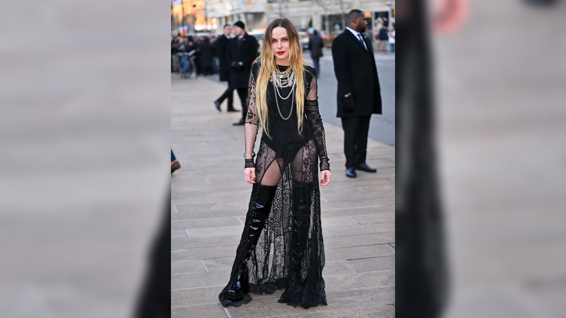 Rebecca Ferguson posa ao ar livre num vestido longo preto transparente com renda e botas altas de verniz.