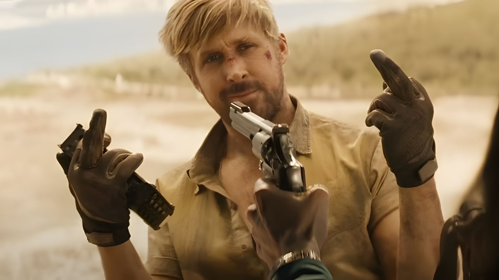 Ryan Gosling com o rosto ferido faz um gesto obsceno enquanto uma arma aponta para o seu rosto