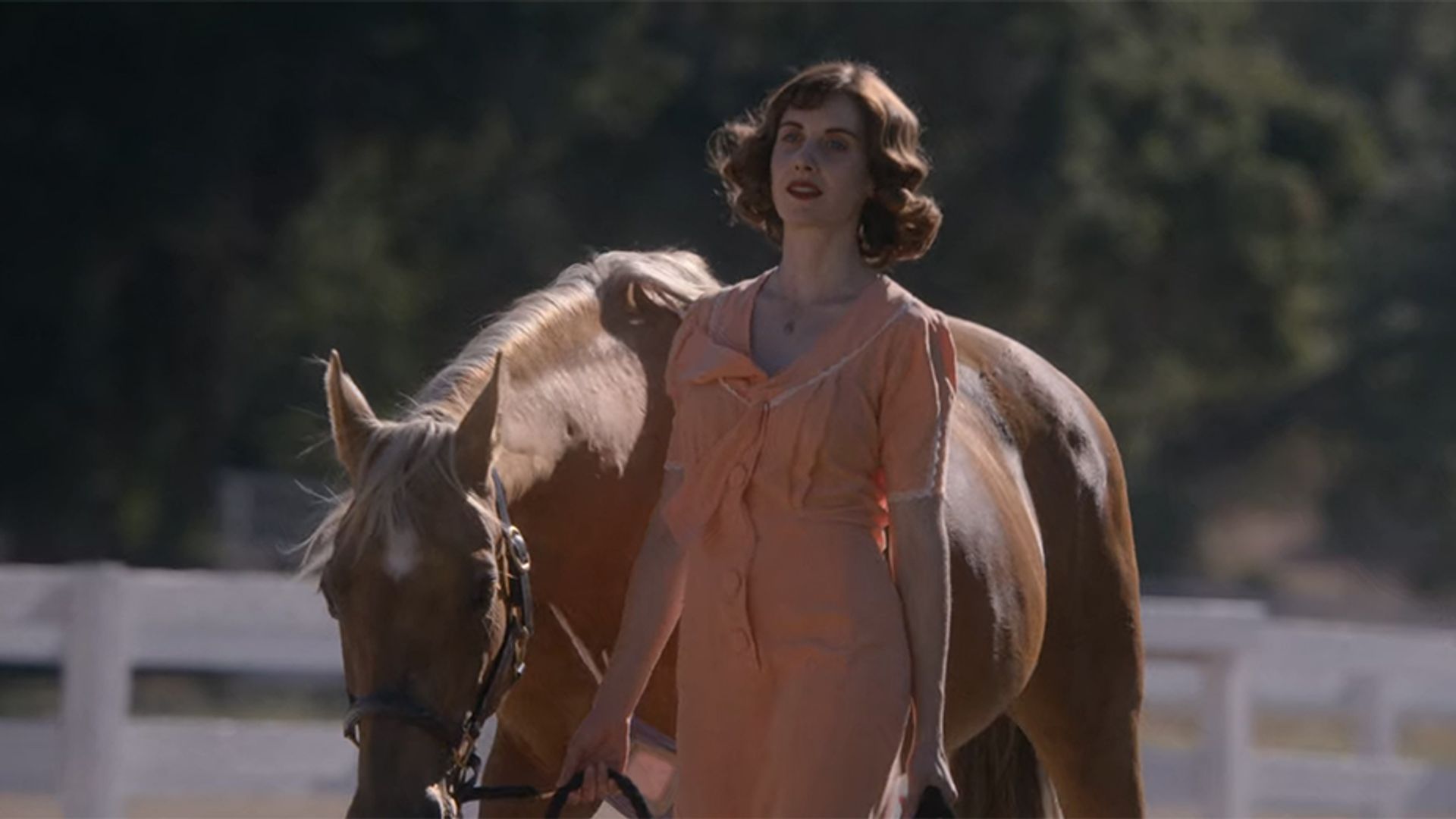 Alison Brie conduzindo um cavalo pelas rédeas, still do filme "Horse Girl"
