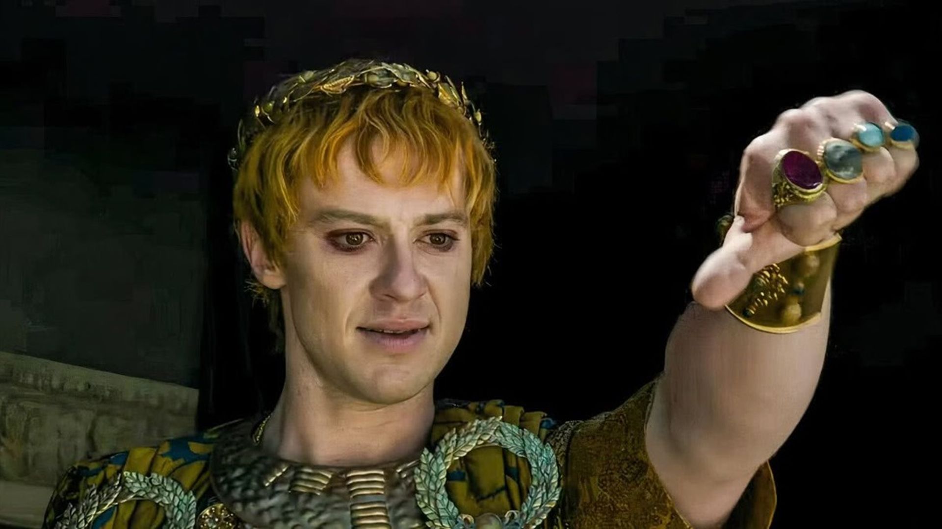 Joseph Quinn com maquilhagem e figurino de imperador romano fazendo gesto de polegar para baixo
