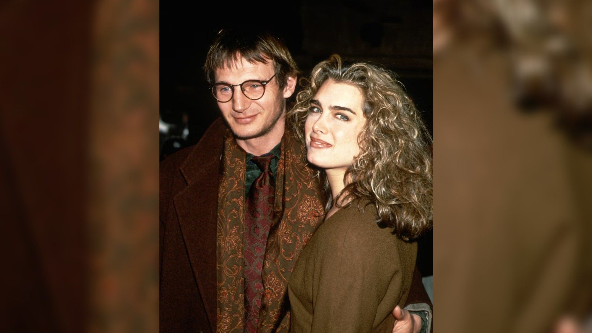 Liam Neeson e Brooke Shields na juventude, abraçados e caminhando em frente