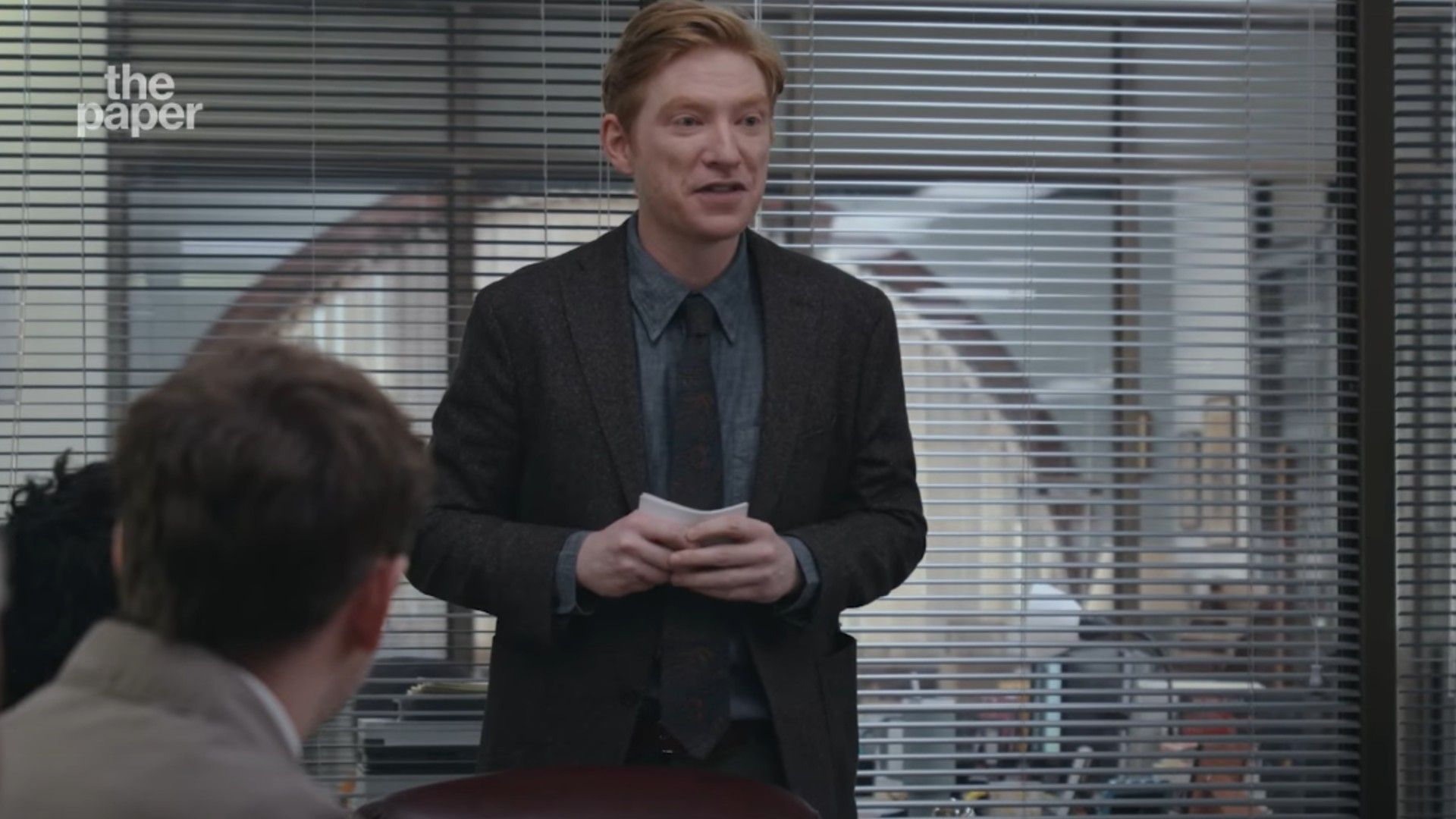 Domhnall Gleeson de fato numa sala de conferências
