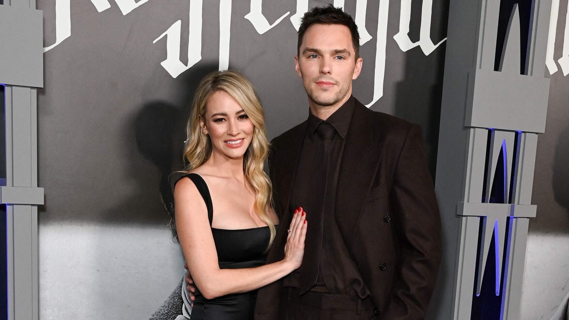 Nicholas Hoult de fato escuro e Bryana Holly de vestido preto posam juntos na passadeira vermelha