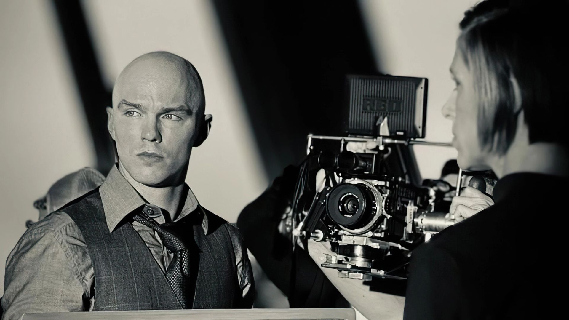 Nicholas Hoult de colete e gravata ao lado de uma câmara de cinema profissional num set de filmagem
