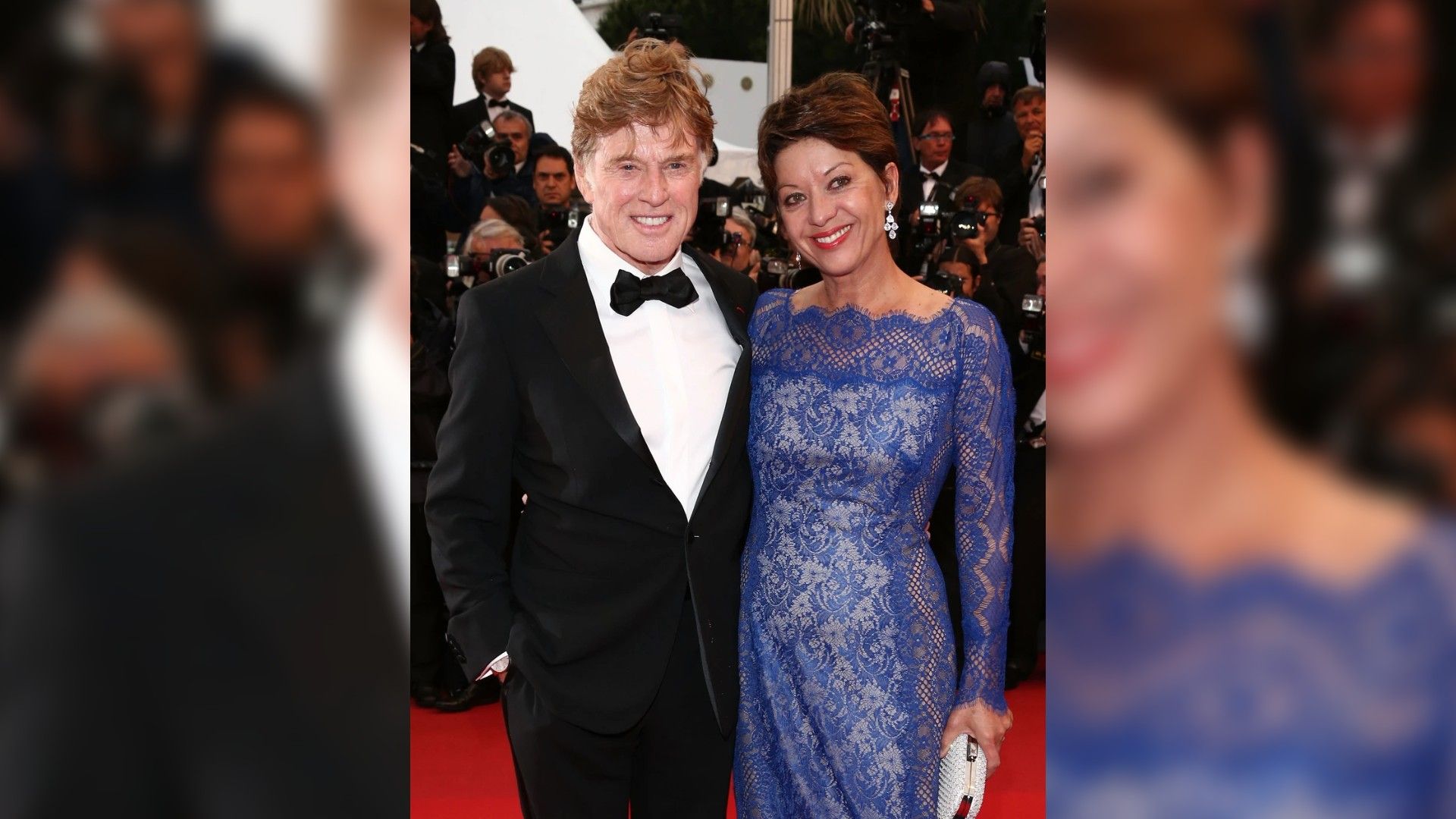 Robert Redford de smoking e Sibylle Szaggars num vestido azul de renda posam na passadeira vermelha rodeados de fotógrafos