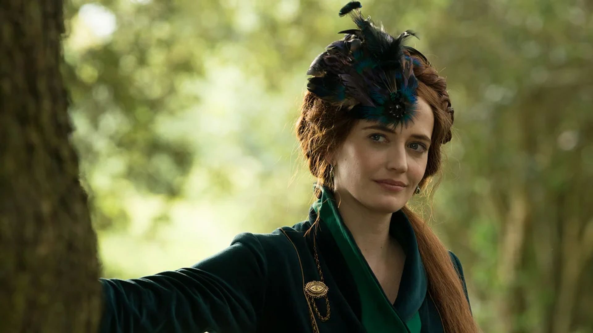 Eva Green num traje verde escuro com ornamentos de penas na cabeça, de pé junto a uma árvore contra um cenário florestal
