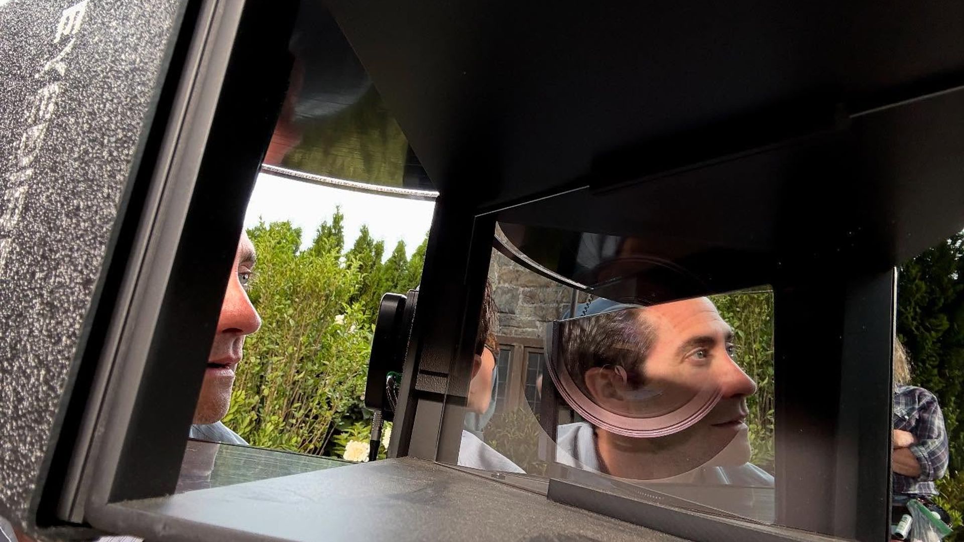 Jake Gyllenhaal olha para equipamento com espelhos e lentes, o seu rosto refletido nas superfícies óticas