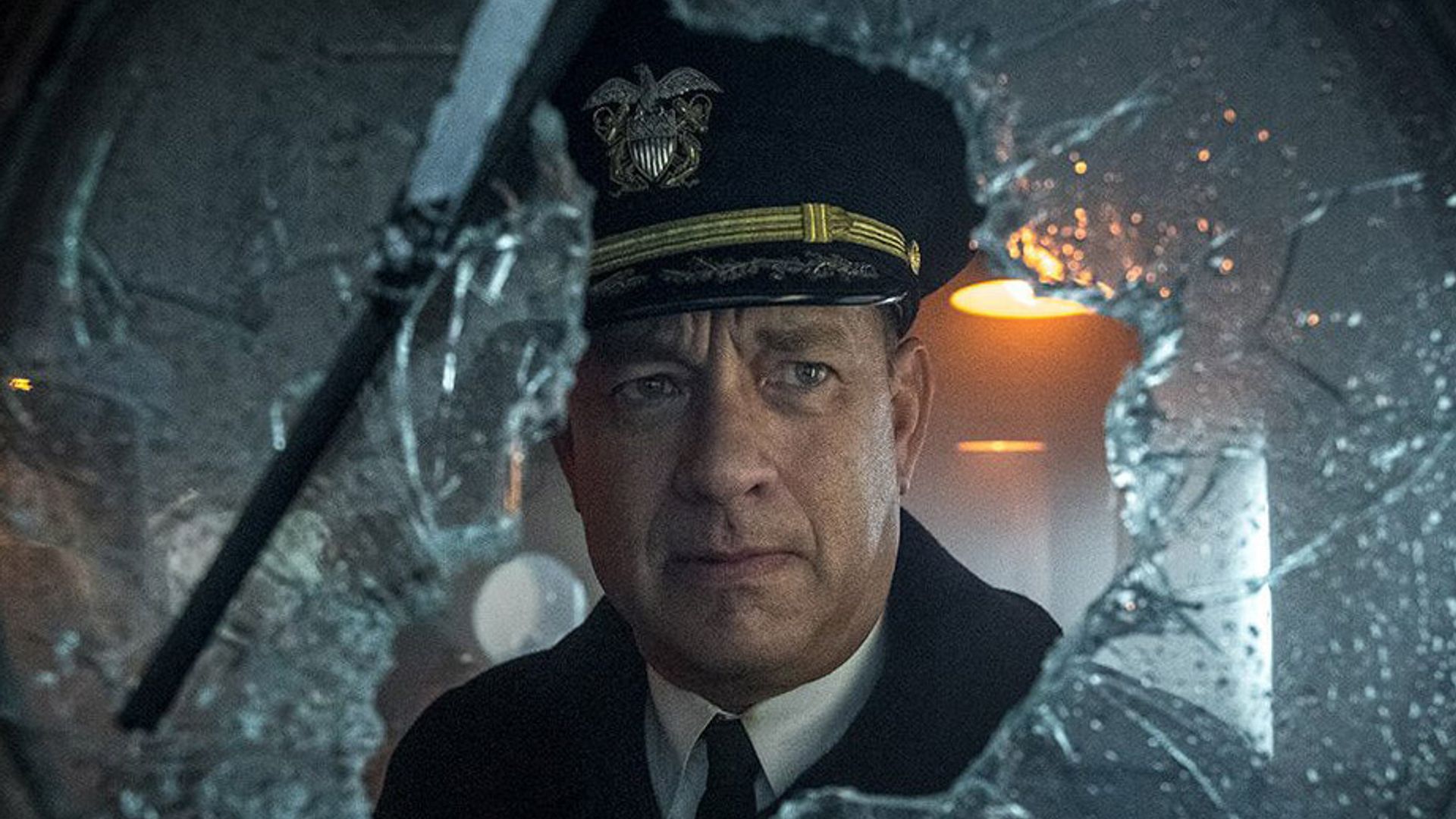 Tom Hanks em uniforme de capitão olha através de vidro partido com uma expressão séria no rosto