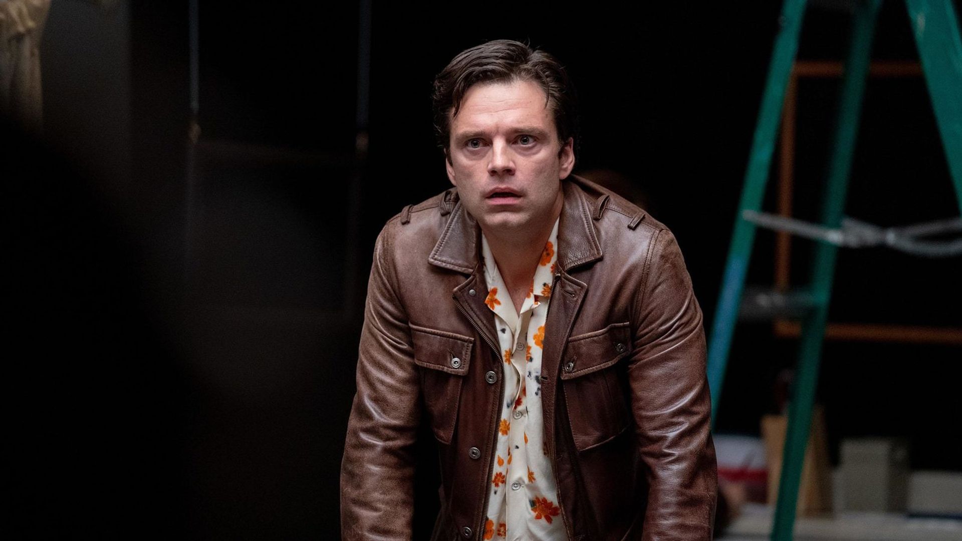 Sebastian Stan com uma jaqueta castanha olhando em frente contra um fundo preto