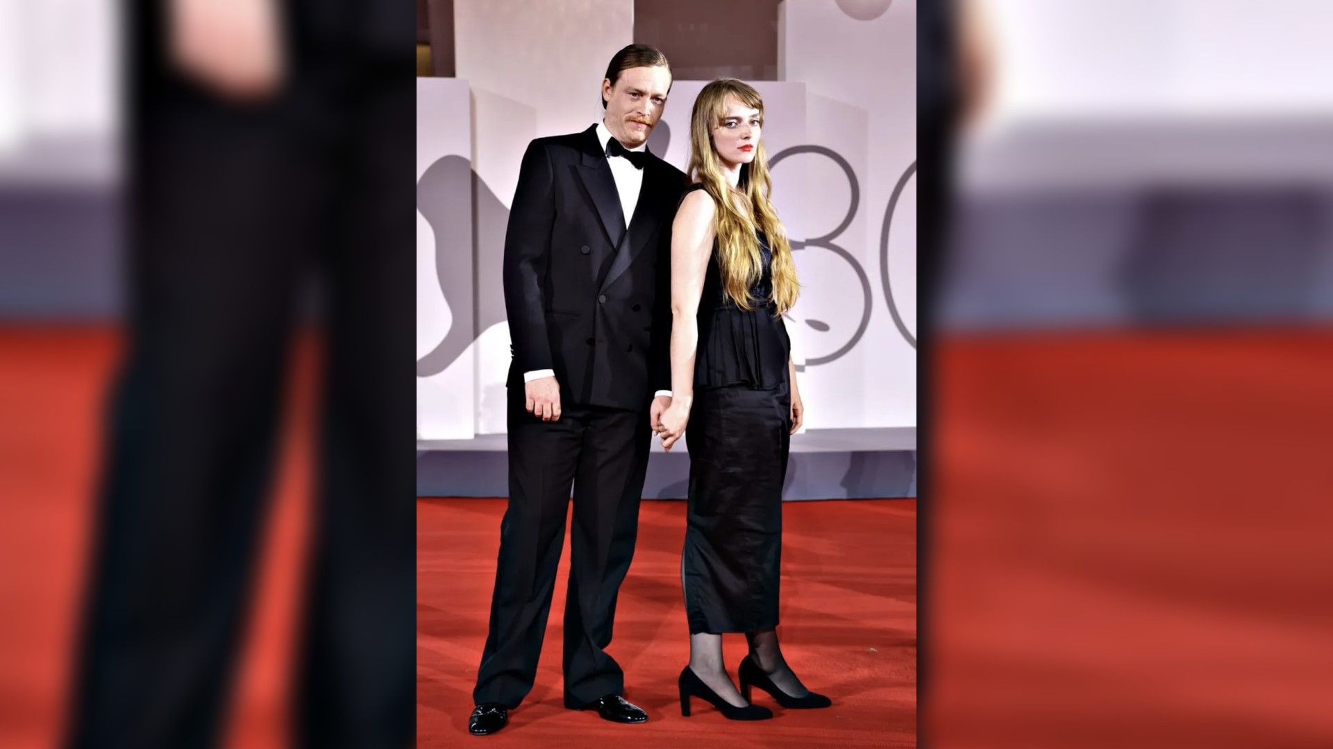 Caleb Landry Jones e Katya Zvereva em traje de gala posam na passadeira vermelha, de mãos dadas
