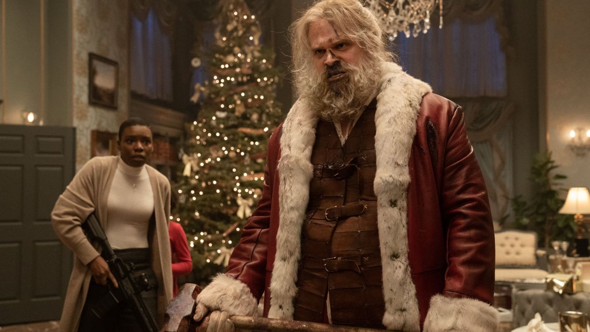 David Harbour em traje de Pai Natal segurando um machado, com interior natalício ao fundo
