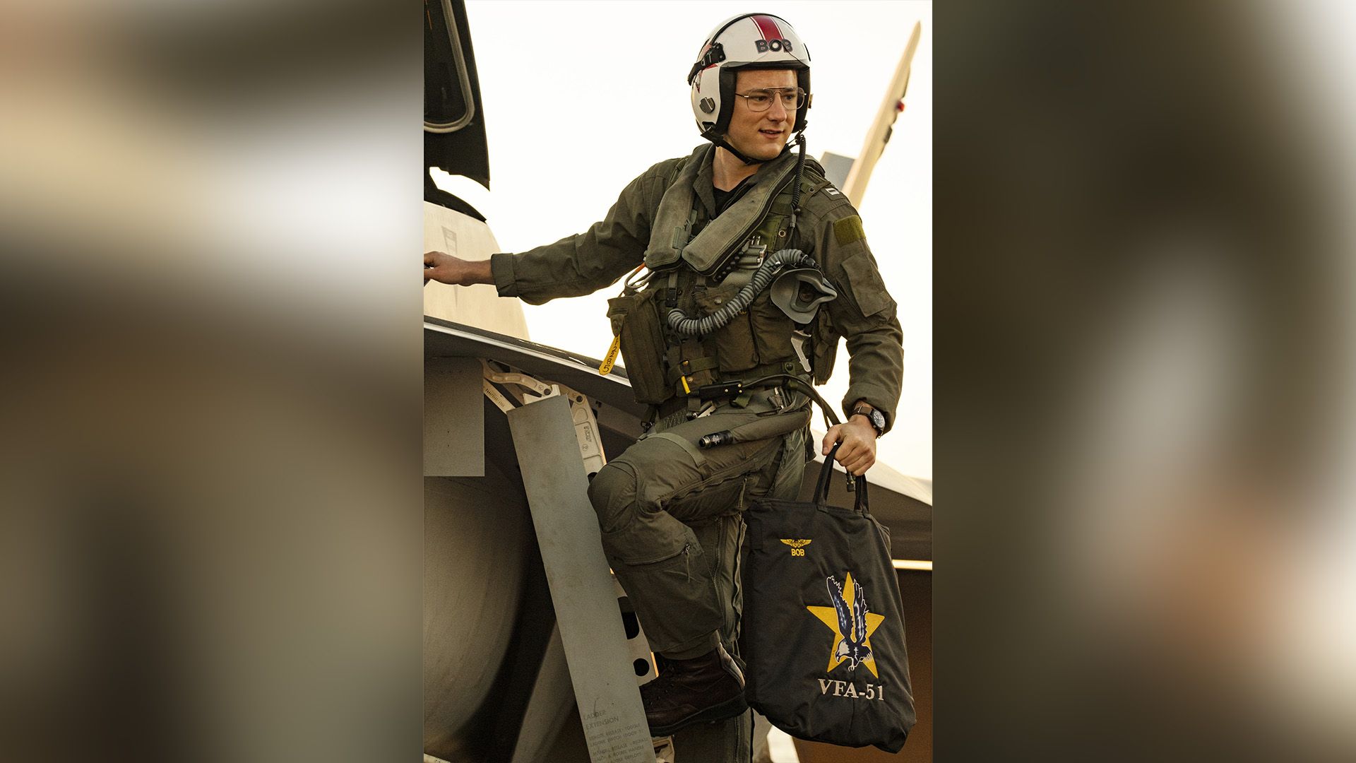 Lewis Pullman em uniforme militar de piloto está no degrau de um caça