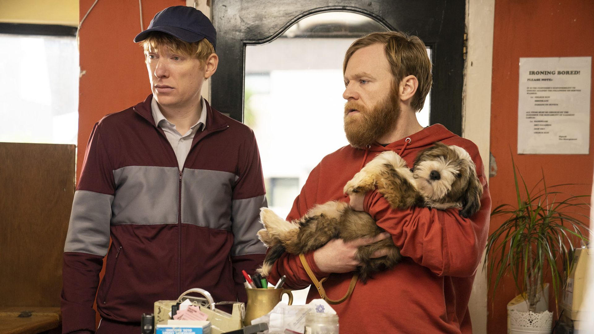 Brian e Domhnall Gleeson em roupa desportiva junto a uma mesa olhando para o lado
