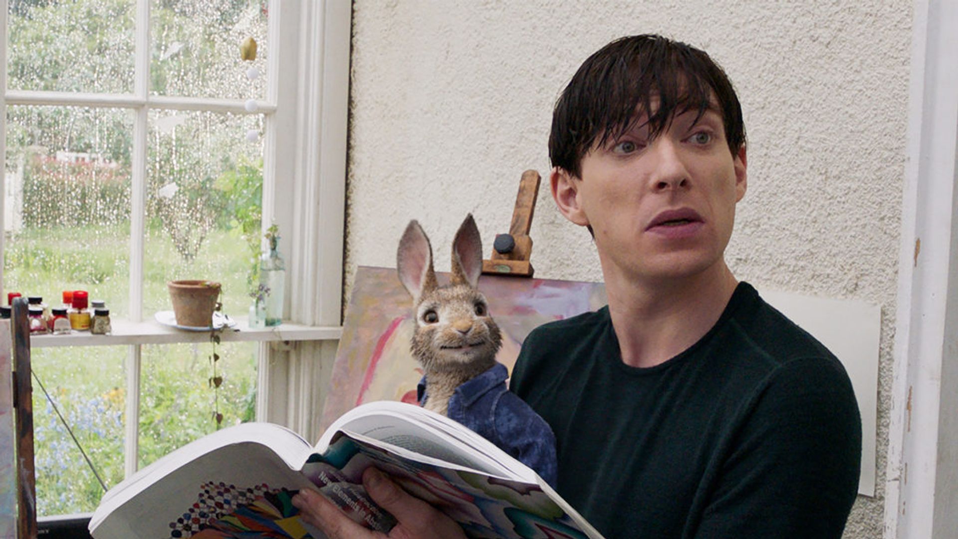 Domhnall Gleeson sentado a ler um jornal com um coelho de brinquedo no colo