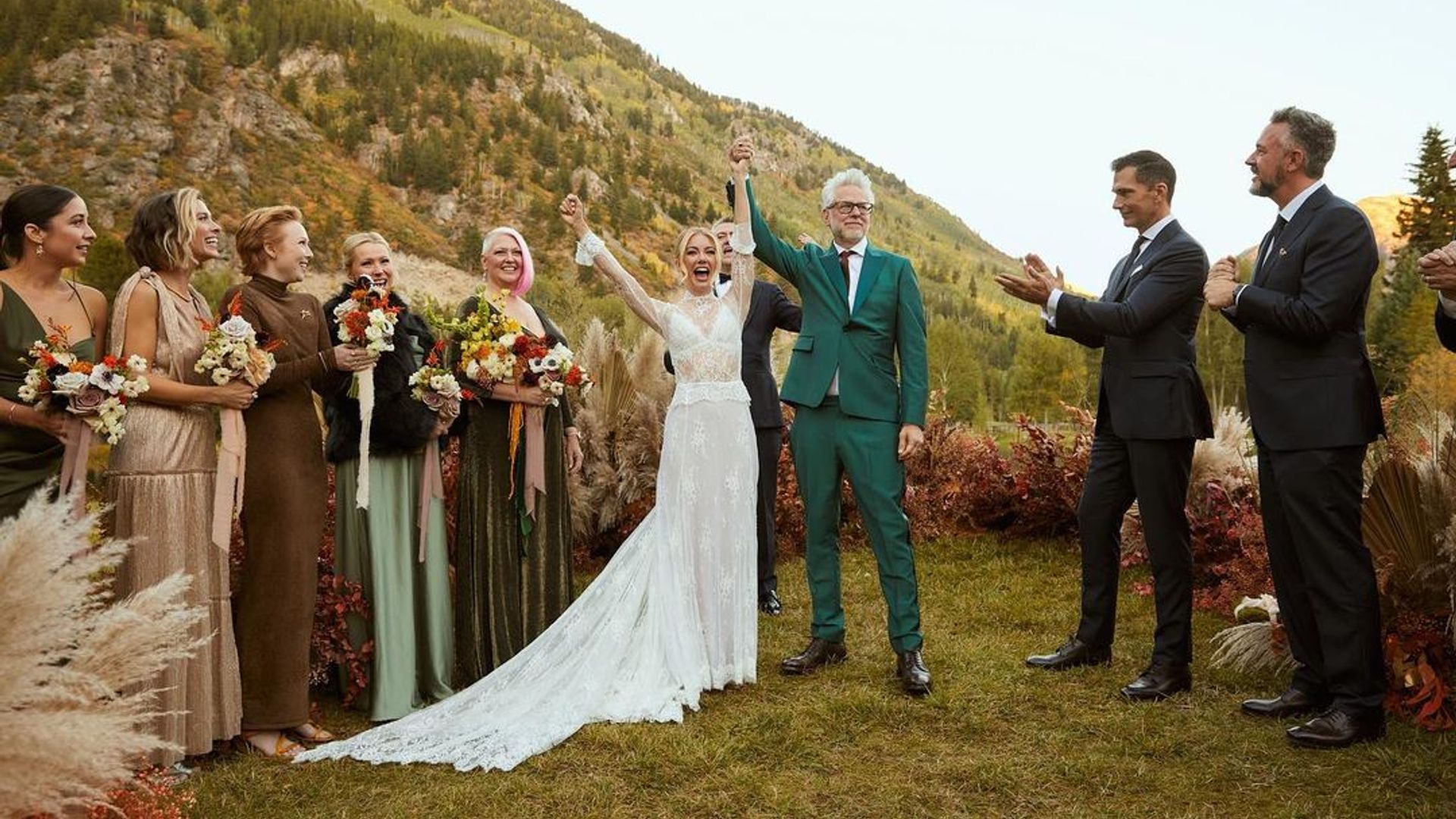 Jennifer Holland e James Gunn em traje de casamento contra um cenário de montanhas pitorescas